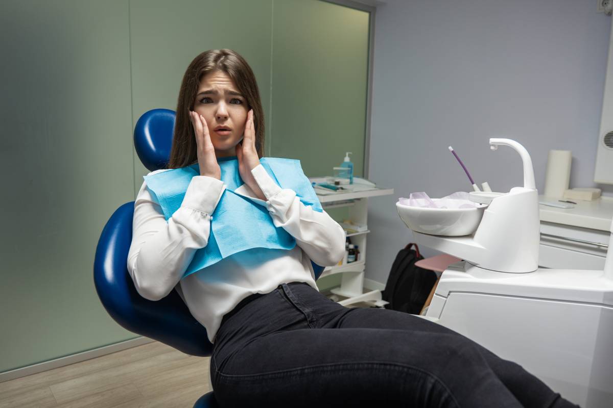 Scared patient sitting in dental chair during examination at dental office desperately touching her face looks frightened.