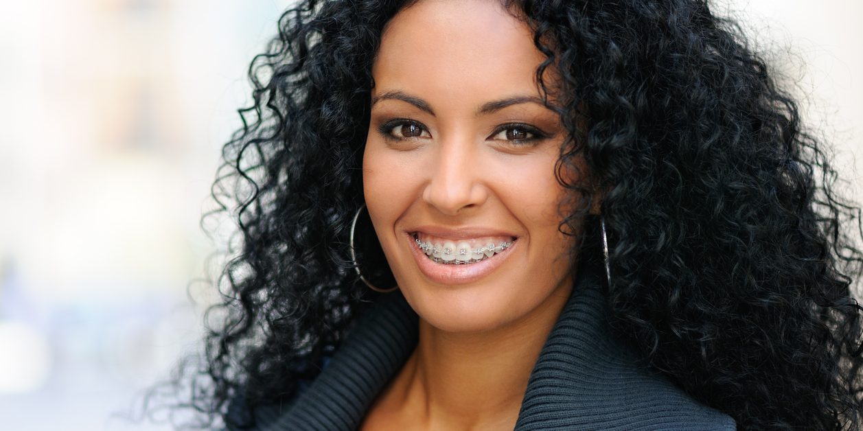 Woman with curly hair and braces smiling.