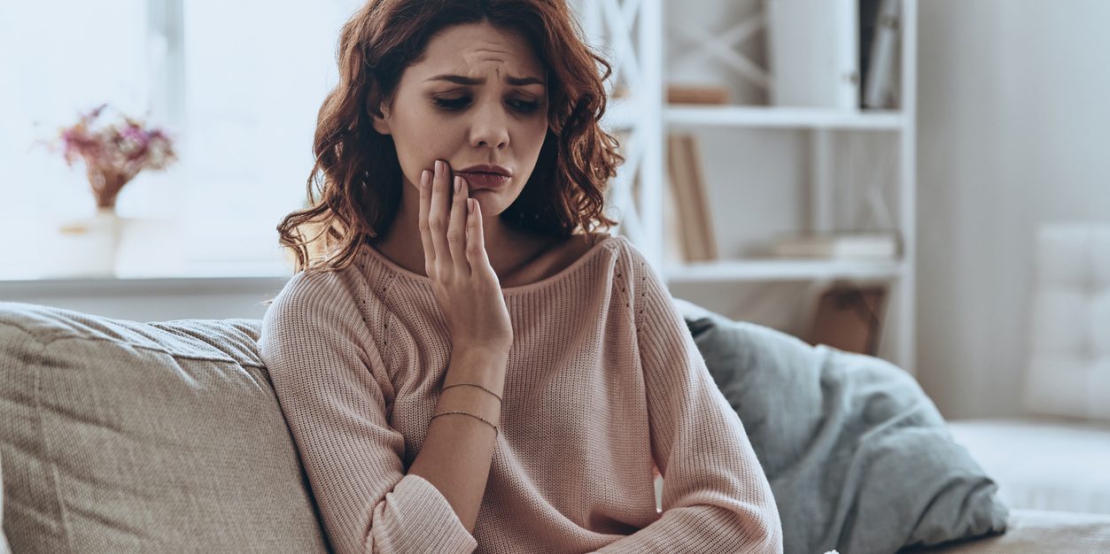 Woman sitting on couch holding face in pain.